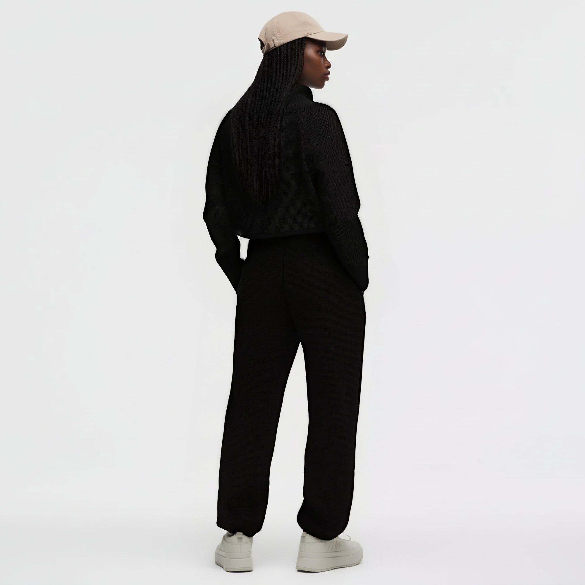 Vue trois-quarts arrière d’un mannequin portant l’ensemble noir GALAYA « SPICA & DENEB », sweat cropped à col montant côtelé vertical (Deneb) et pantalon taille haute waffle (Spica), mains dans les poches, dos droit, casquette beige clair, silhouette monolithique noire sur fond blanc studio, contraste révélant subtilement les textures.