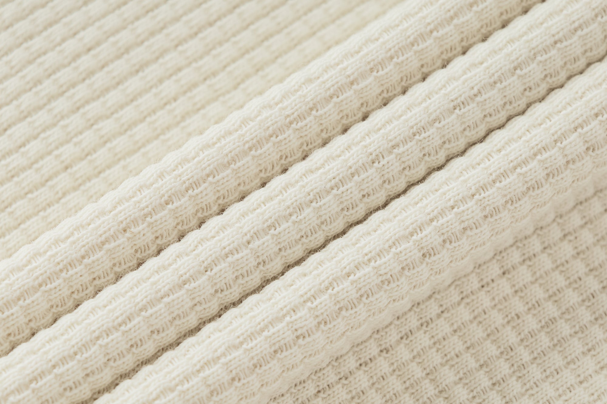 Gros plan sur la texture côtelée verticale du tissu ivoire de la collection GALAYA « SPICA & DENEB », maille rib fine et régulière, matière souple et structurée, lumière douce soulignant le relief et la qualité du textile.