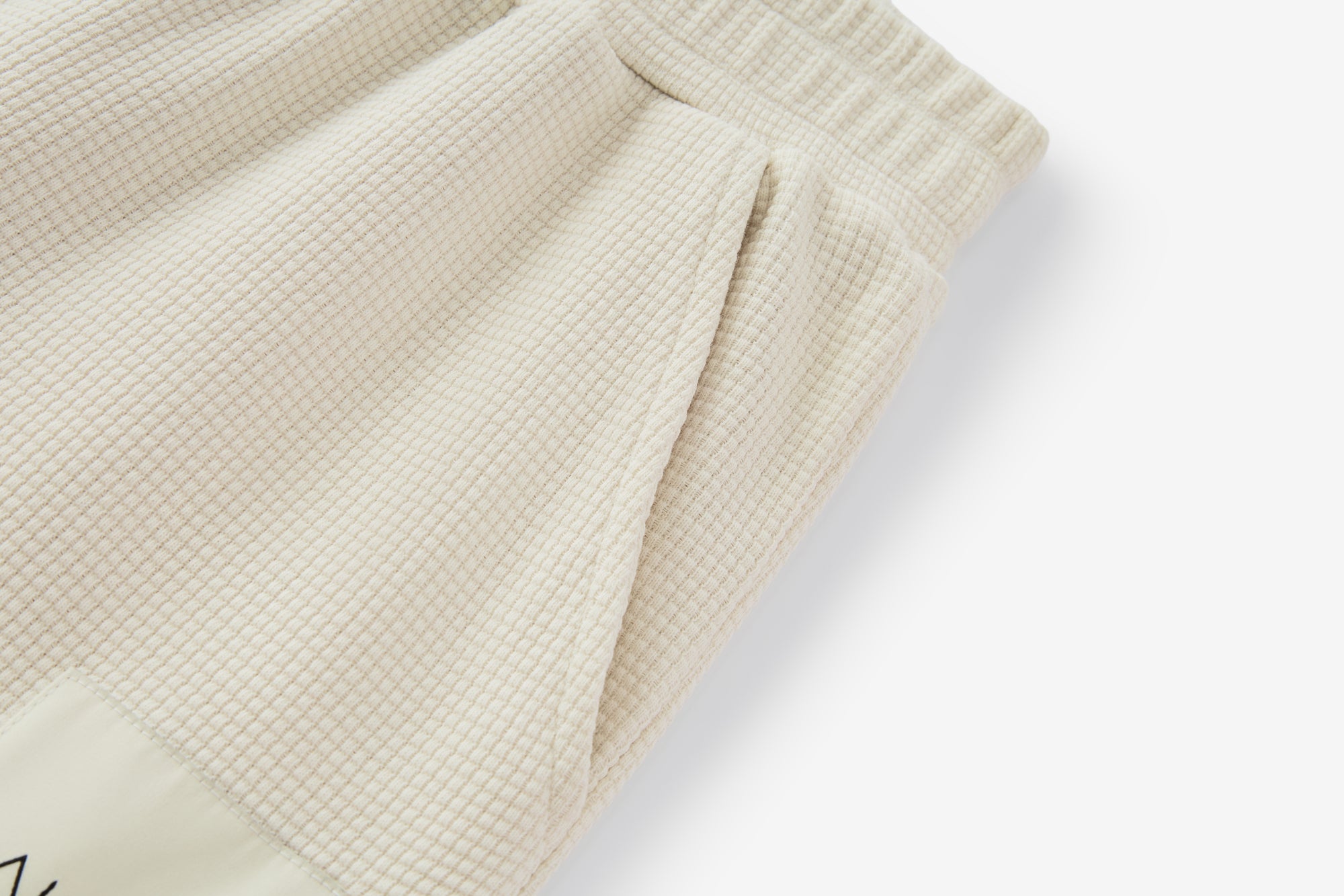 Gros plan sur la taille d’un pantalon ivoire de la collection GALAYA "SPICA &amp; DENEB", maille texturée côtelée, couture ton sur ton et double épaisseur assurant maintien confortable et finition soignée, sur fond blanc studio.