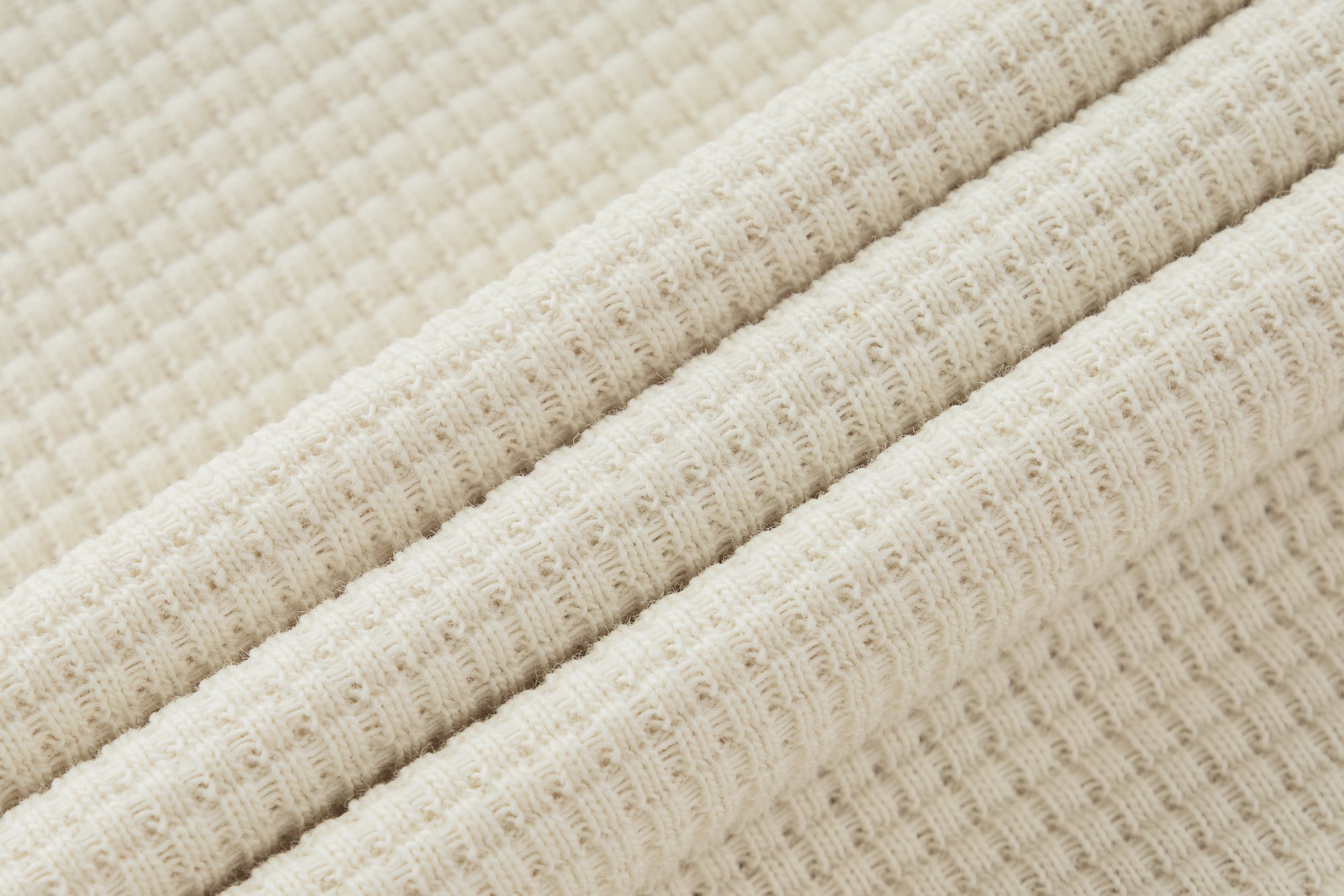 Gros plan sur le tissu ivoire de la collection GALAYA "SPICA &amp; DENEB", maille texturée côtelée et nid d’abeille, matière épaisse et douce, lumière diffuse soulignant la qualité, la structure et l’aspect naturel du textile.